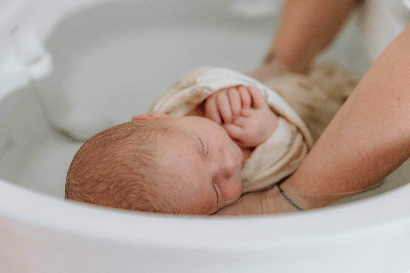 Nouveau-né endormi dans le bain, enveloppé dans son lange, la tête soutenue par une main — Entre Deux