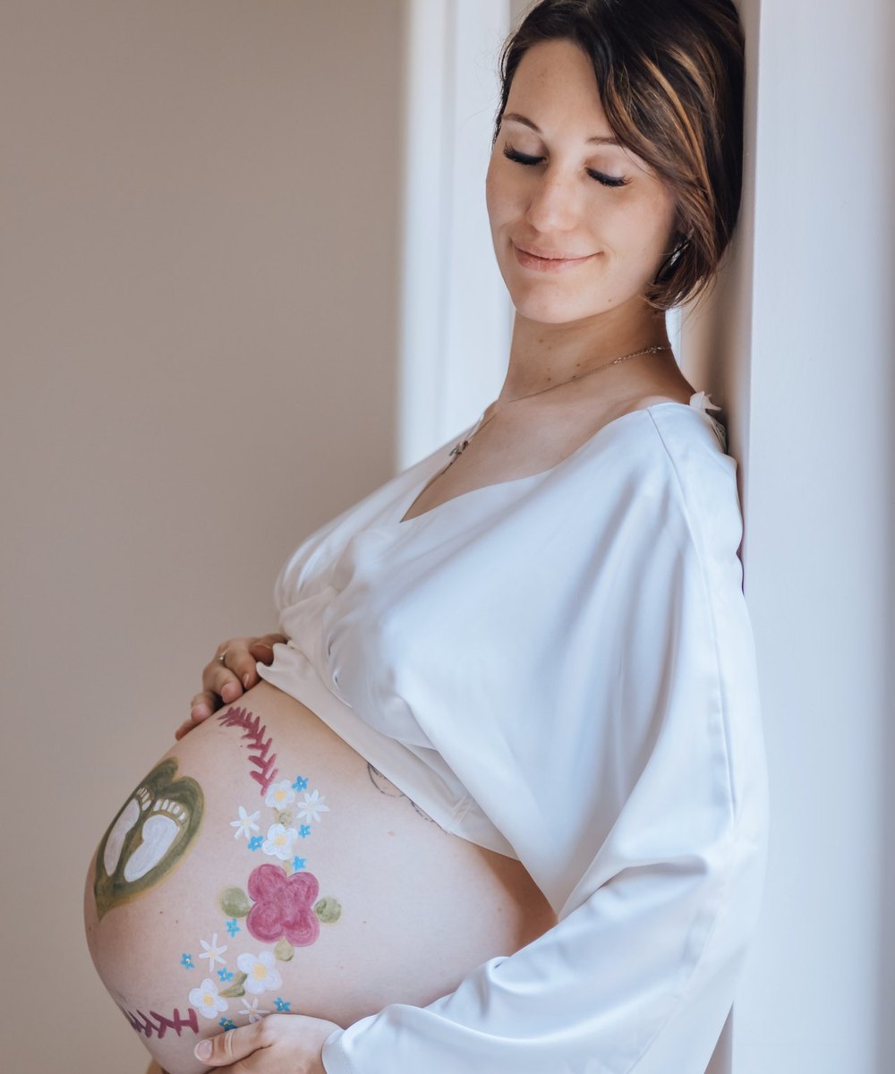 Future maman en peignoir blanc, le ventre peint de fleurs et de petits pieds — Entre Deux