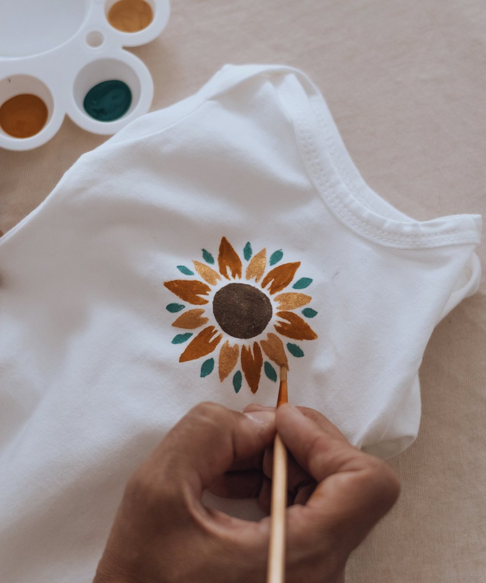 Vêtement de naissance peint à la main d'un tournesol, pinceau et palette de couleurs — Entre Deux
