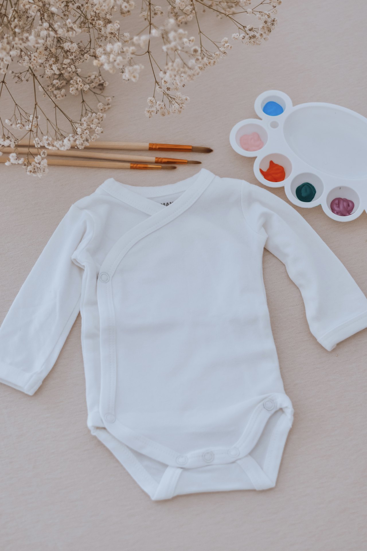 Vêtement de bébé encore vierge, pinceaux et palette de couleurs prêts pour l'atelier