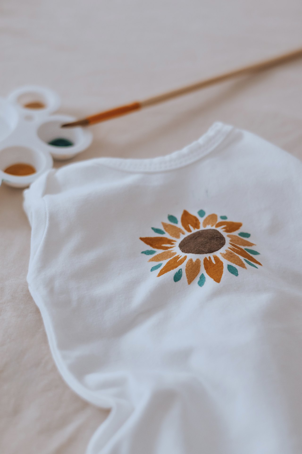 Tournesol peint à la main sur un vêtement, palette et pinceau posés à côté