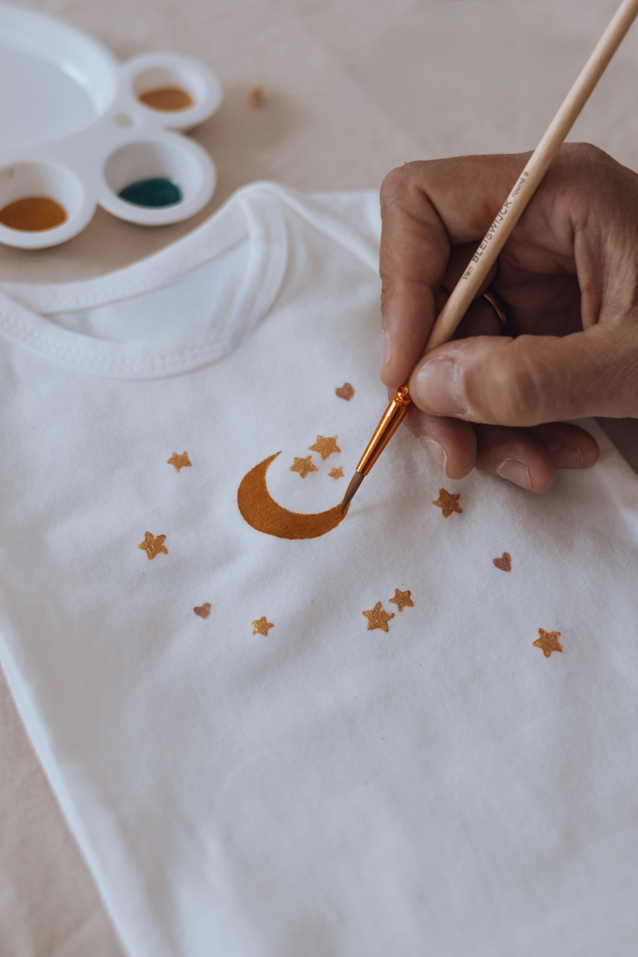 Main peignant une lune et des étoiles dorées sur un vêtement de bébé pendant un atelier — Entre Deux