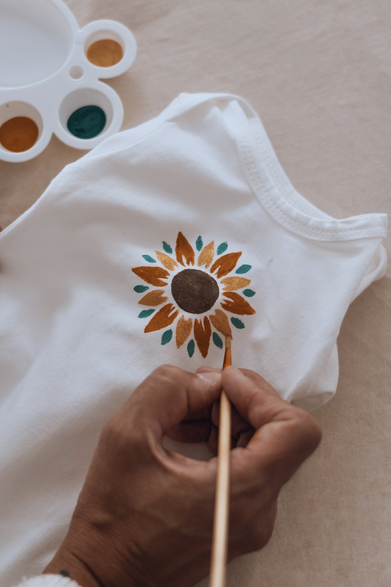 Main peignant les pétales d'un tournesol sur un vêtement, palette de peintures textile