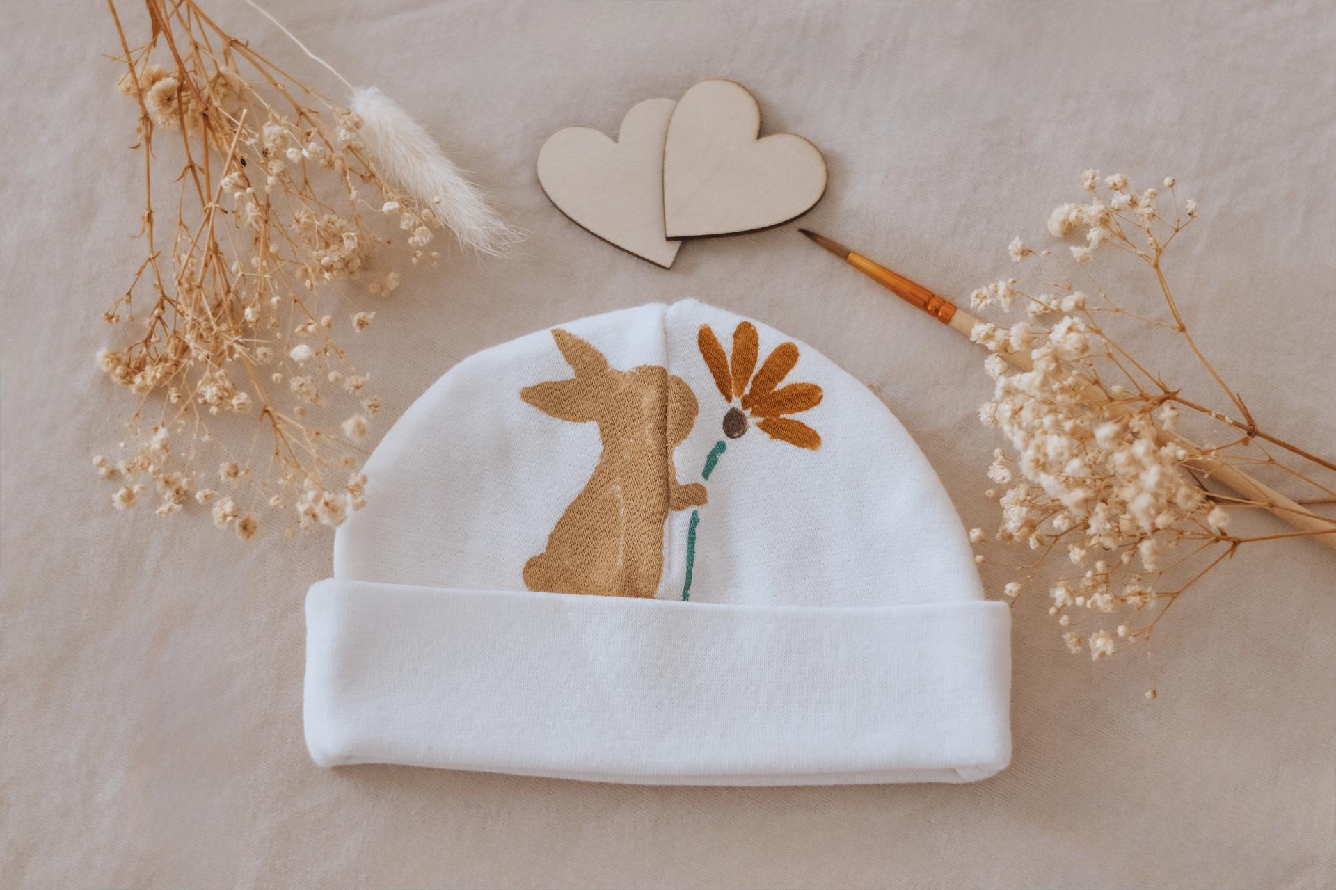 Bonnet de naissance peint d'un petit renard et d'une fleur, entouré de fleurs séchées