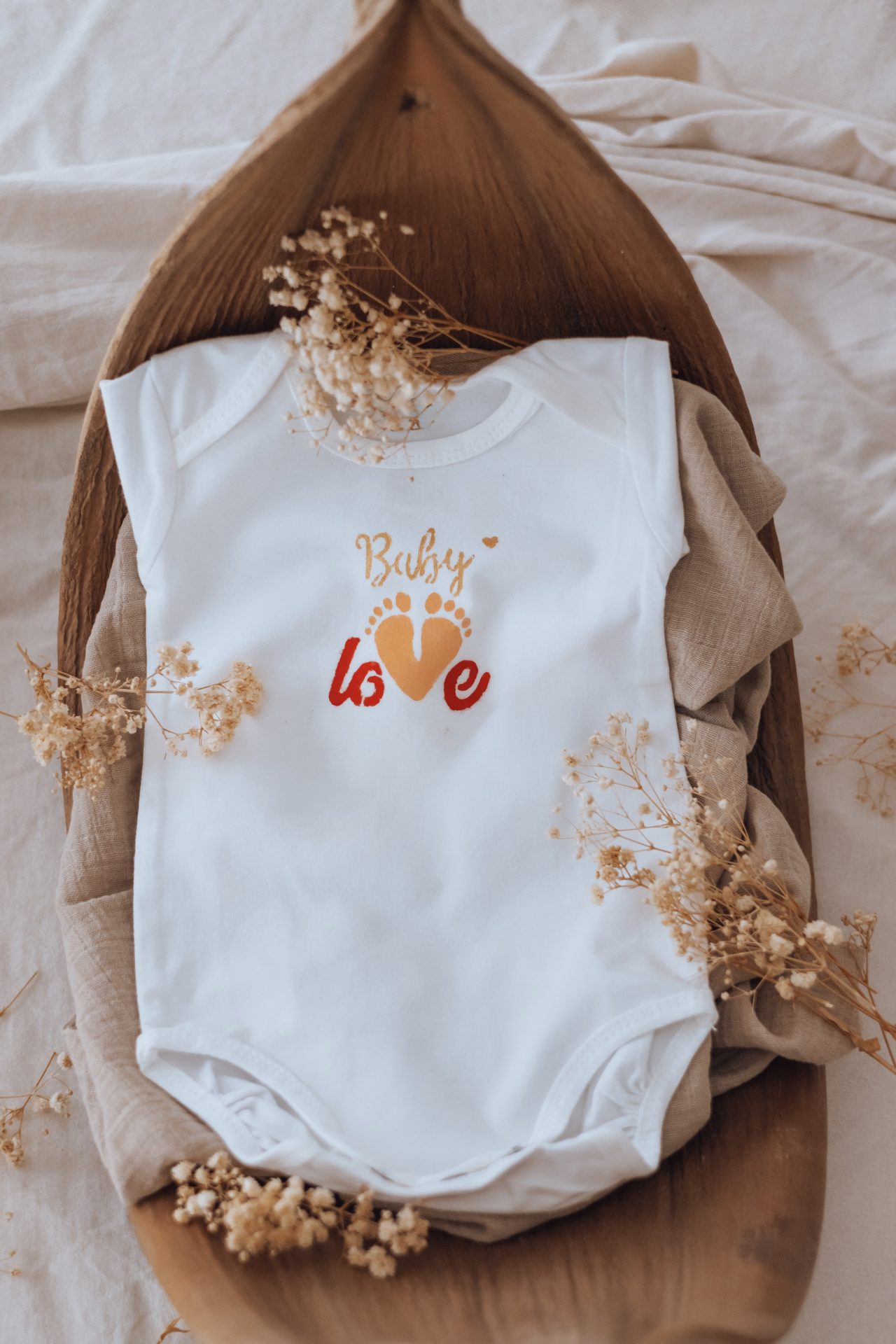 Vêtement « Baby love » terminé, posé sur un plateau en bois avec des fleurs séchées