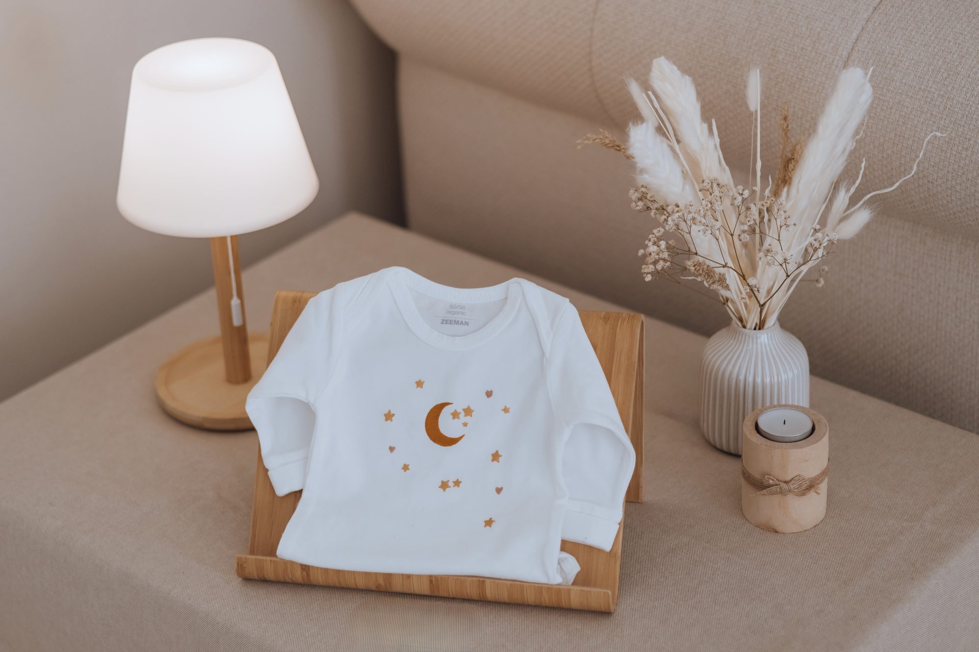 Vêtement de bébé peint d'une lune et d'étoiles dorées, posé sur un présentoir en bois — atelier Entre Deux