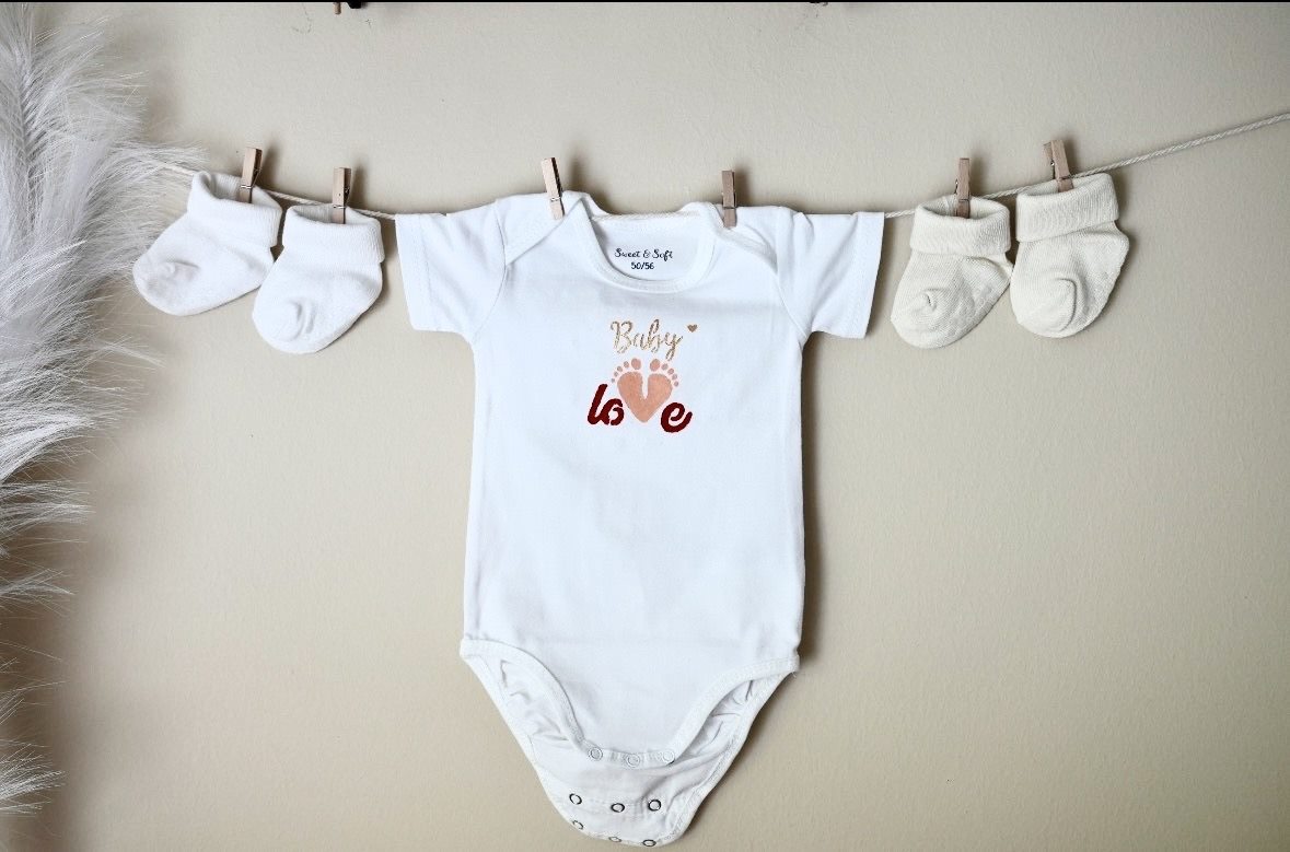 Vêtement « Baby love » peint à la main, suspendu sur une cordelette entre deux paires de chaussons — Entre Deux